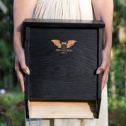 Black two-chamber bat house being held by hands