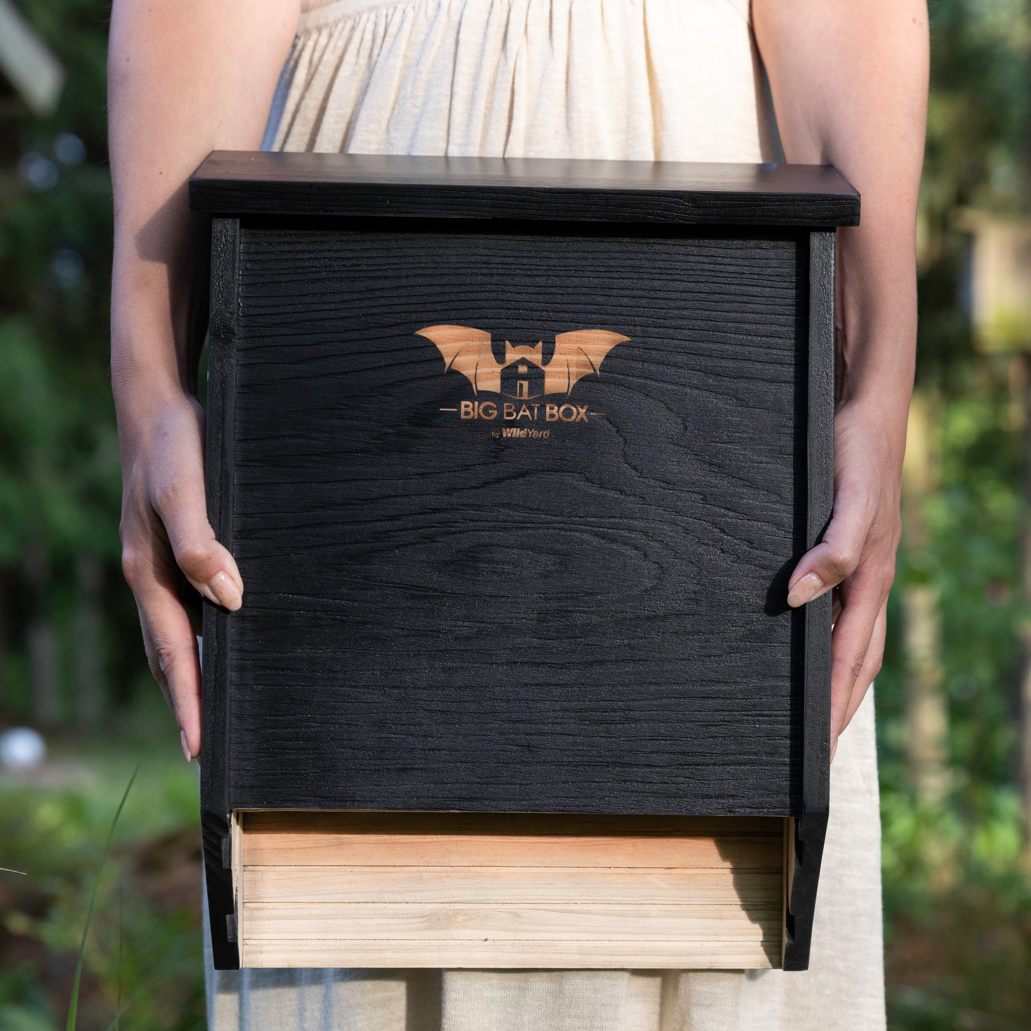 Black two-chamber bat house being held by hands
